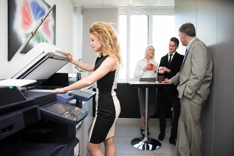 Colleagues talking while a coworker uses the office copier