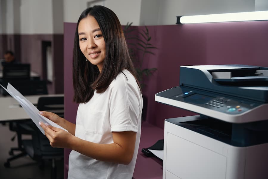 Office employee holding documents next to a multifunction copier